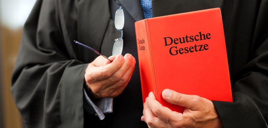 Das Bild zeigt ein Gesetzbuch in der Hand eines Richters